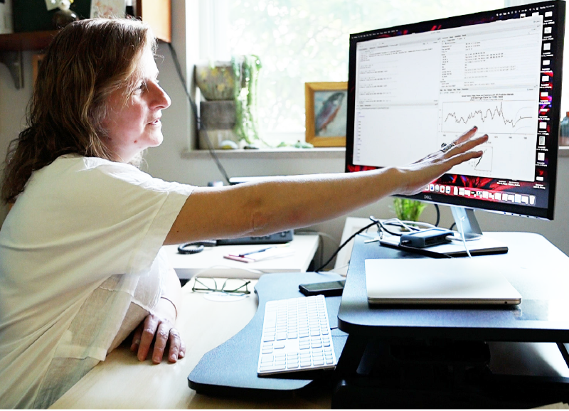 Woman in an office setting pointing at analytics on a computer monitor.